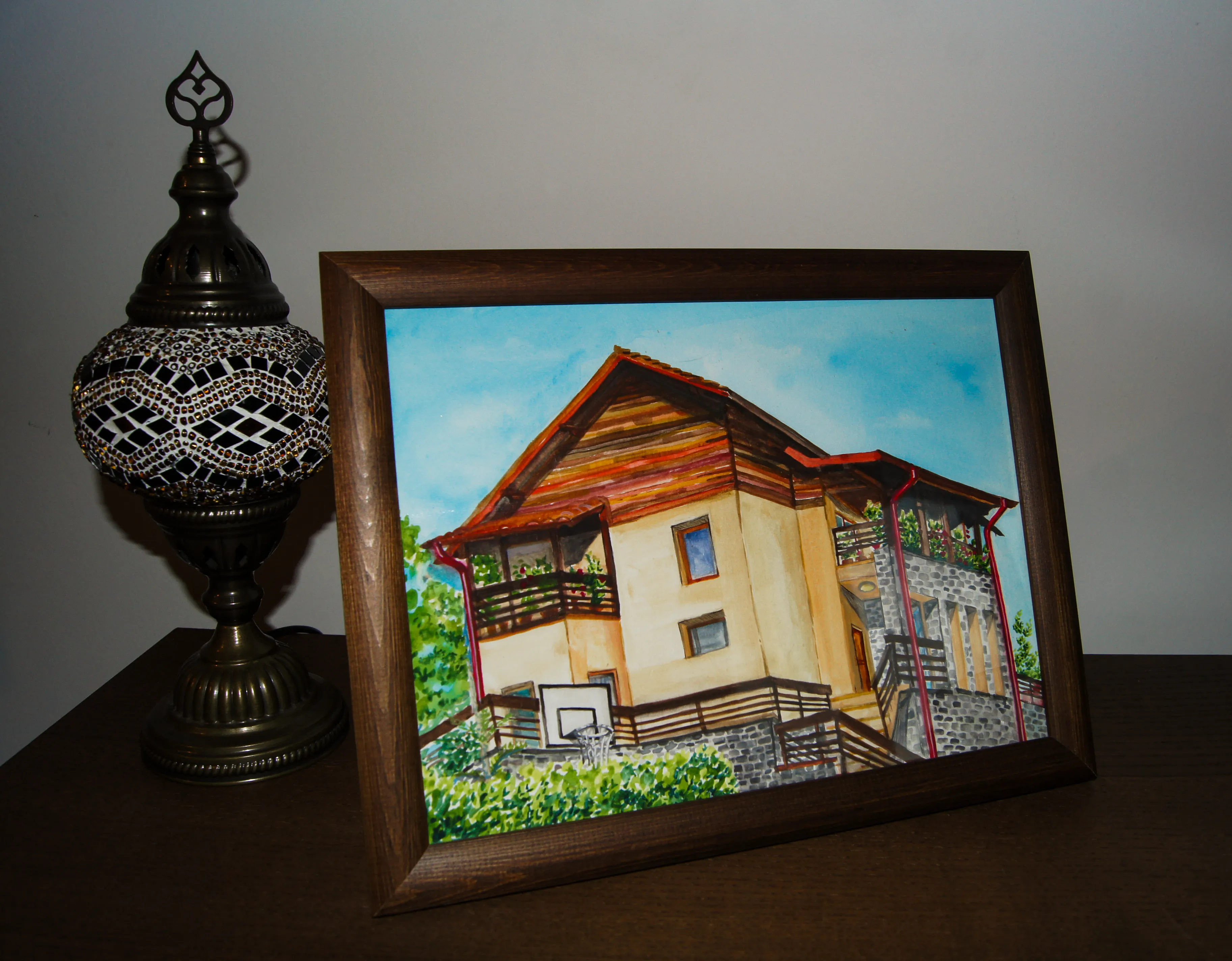 The finished watercolor in a dark wooden frame, propped on a table beside a mosaic glass lamp.
