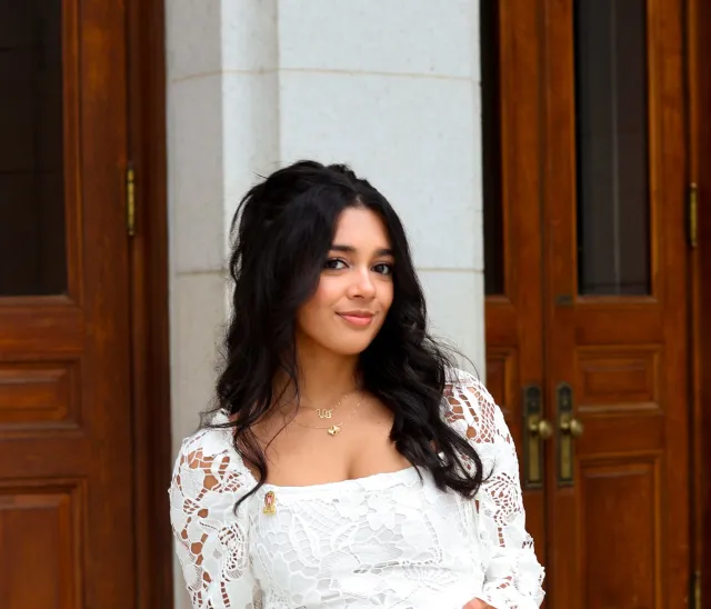 Vanya Srivastava standing in front of tall wooden doors, wearing a white lace dress.