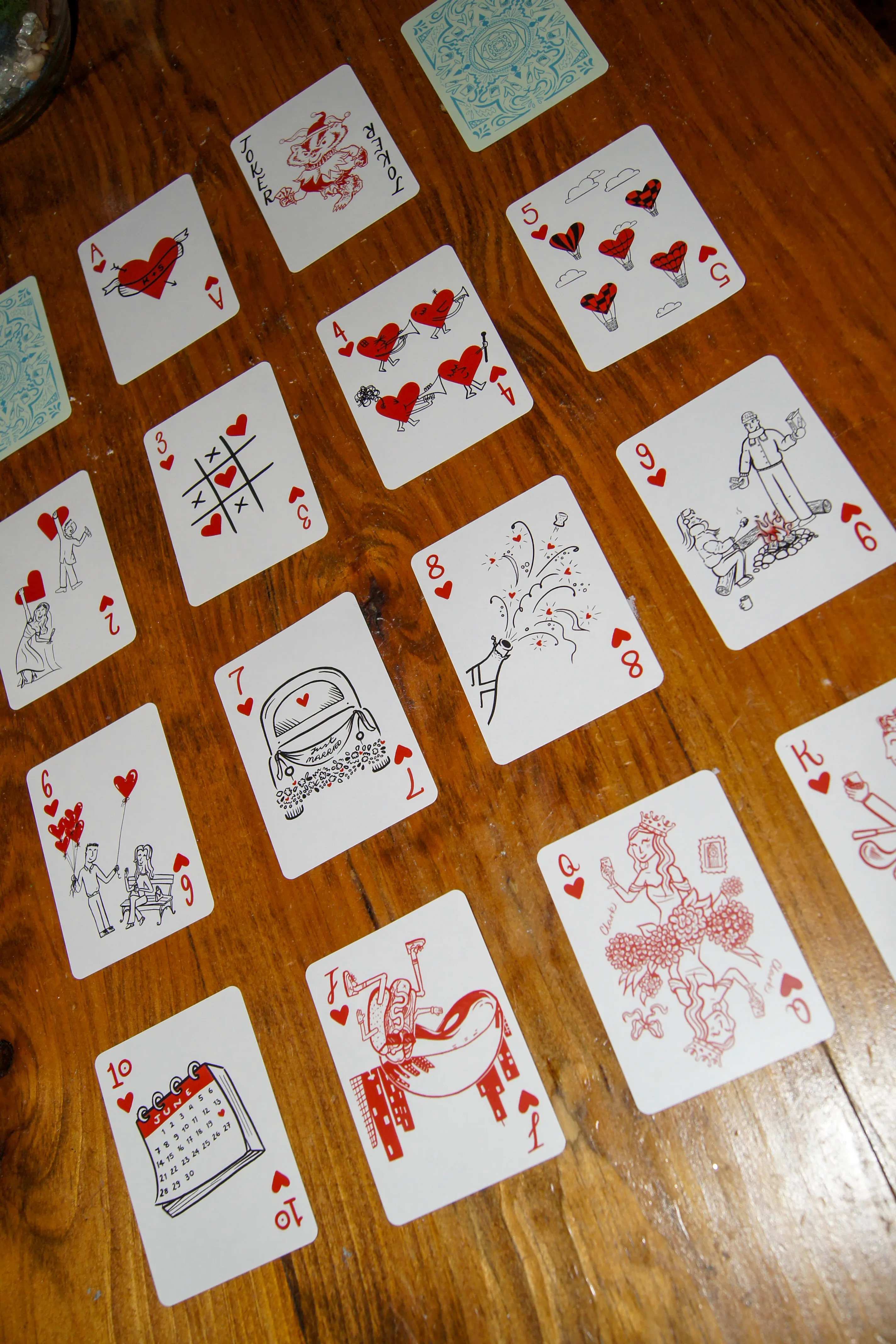The full suit of hearts laid out in rows, each card hand-illustrated in red — hot air balloons, a wedding calendar, a decorated getaway car, and a bride as the queen.